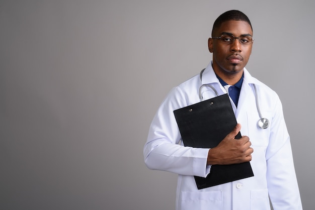 Young handsome African man doctor on gray