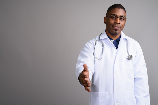 Young handsome African man doctor on gray