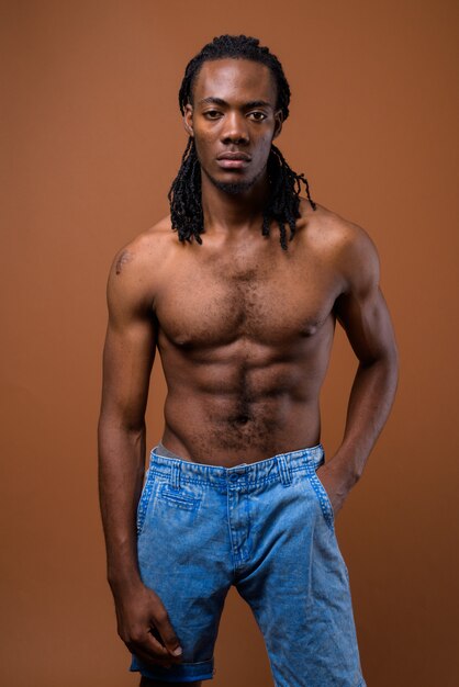 Young handsome African man shirtless against brown background