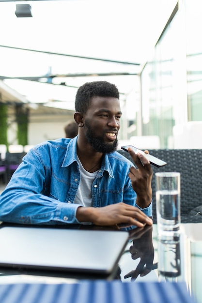 Молодой красивый африканский мужчина разговаривает по телефону на громкоговорителе в кафе