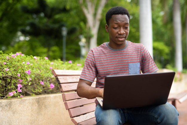 Young handsome African man using laptop in park