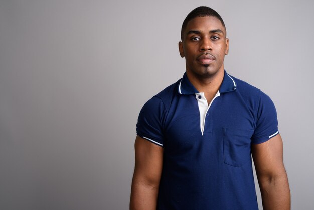 Young handsome African man wearing blue polo shirt on gray