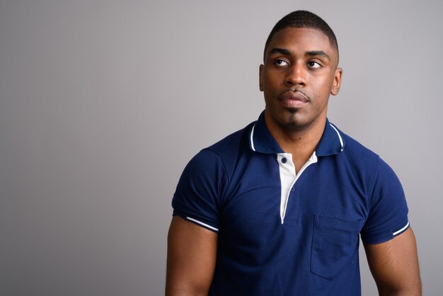 Young handsome African man wearing blue polo shirt on gray