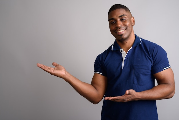 Young handsome African man wearing blue polo shirt on gray