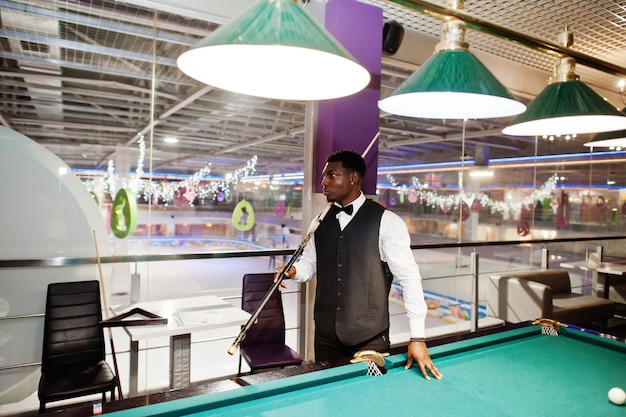 Young handsome african man wearing white shirt black vest and bow tie play pool billiard