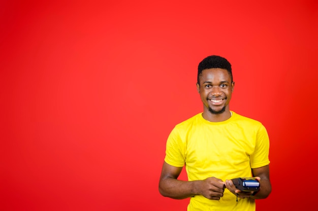 A young handsome african man wearing yellow cloth feeling excited as he holds his point of sales machine