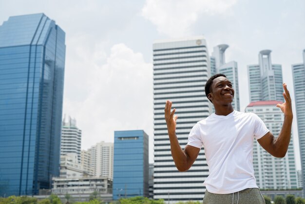 Young handsome African man with arms raised outdoors with cityscape