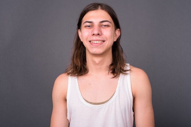  young handsome androgynous man with long hair against gray wall