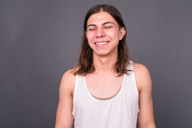 Young handsome androgynous man with long hair against gray wall