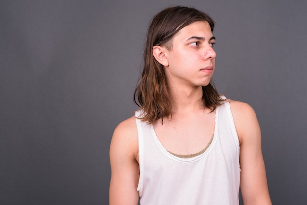  young handsome androgynous man with long hair against gray wall