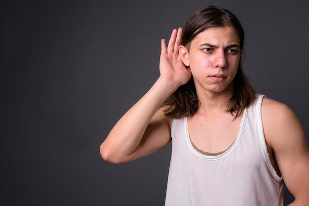 Young handsome androgynous man with long hair against gray wall