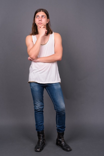  young handsome androgynous man with long hair against gray wall