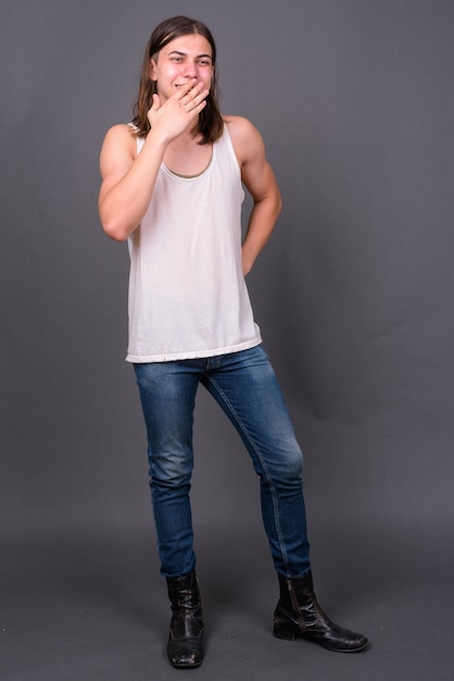  young handsome androgynous man with long hair against gray wall