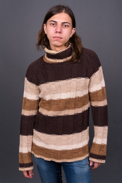  young handsome androgynous man with long hair ready for winter against gray wall