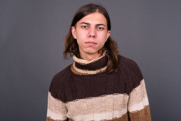  young handsome androgynous man with long hair ready for winter against gray wall