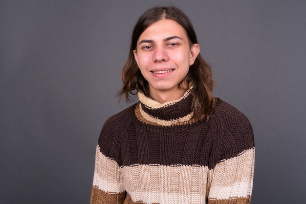  young handsome androgynous man with long hair ready for winter against gray wall