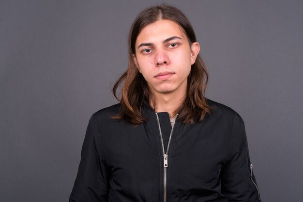  young handsome androgynous man with long hair wearing jacket against gray wall