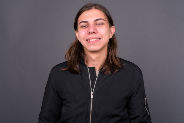  young handsome androgynous man with long hair wearing jacket against gray wall