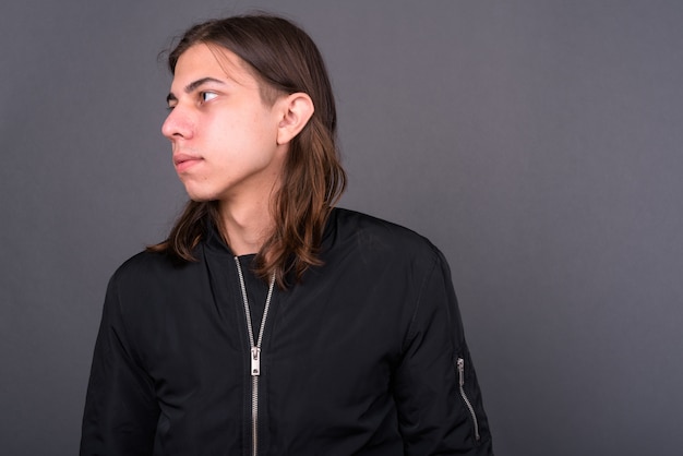  young handsome androgynous man with long hair wearing jacket against gray wall