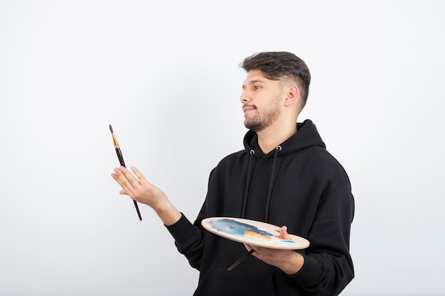 Young handsome artist holding paintbrushes and palette with colors