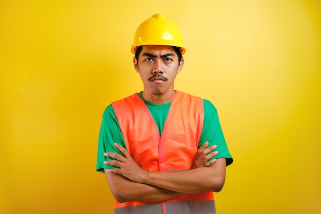 Giovane bell'uomo asiatico indiano lavoratore che indossa gilet arancione e casco di sicurezza scettico e nervoso, espressione di disapprovazione sul viso con le braccia incrociate. persona negativa.