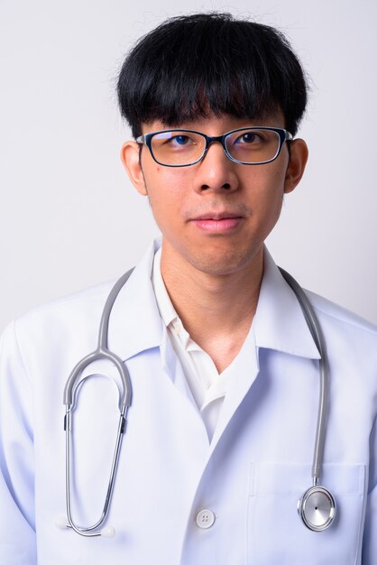 young handsome Asian man doctor against white wall