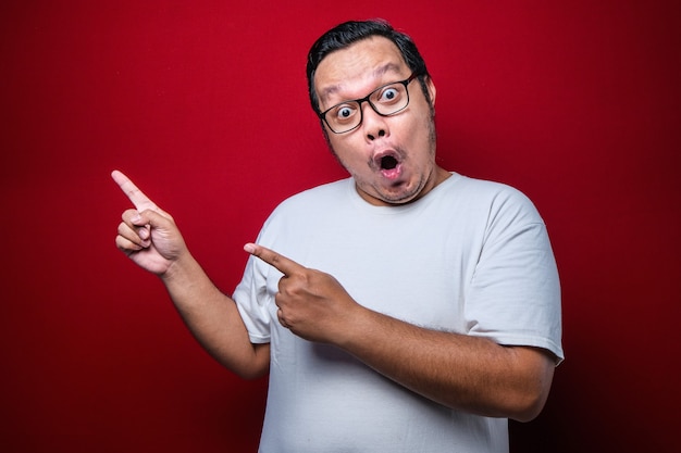 Photo young handsome asian man pointing with fingers to the side afraid and shocked with surprise and amazed expression, fear and excited over red background