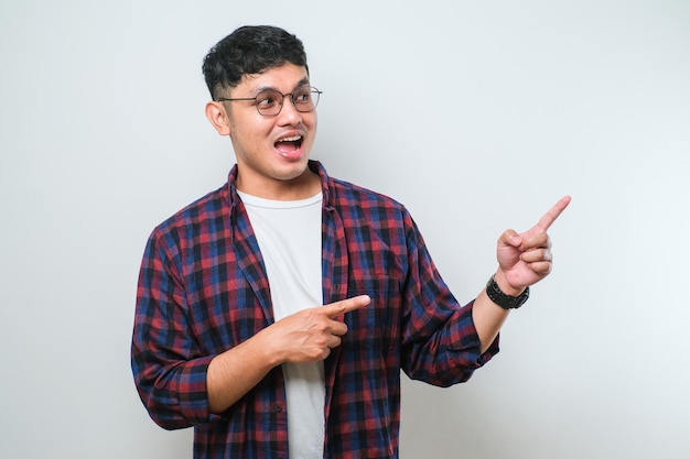 Young handsome asian man pointing with hand finger to the side looking at the camera