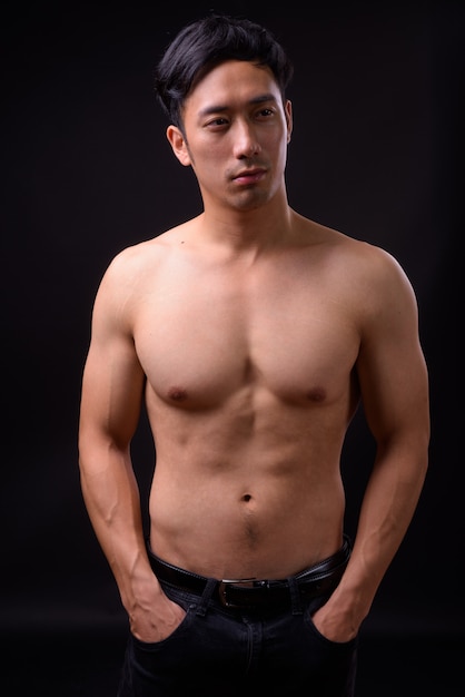 Young handsome Asian man shirtless on black wall