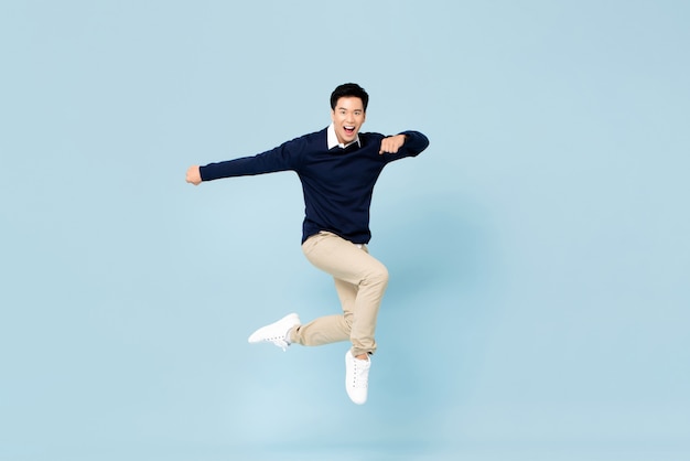 Photo young handsome asian man smiling and jumping in mid-air on light blue wall