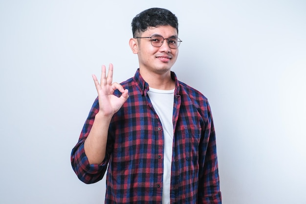 Photo young handsome asian man wearing casual shirt and glassessmiling doing ok sign thumb up with fingers excellent sign