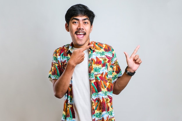 Young handsome asian man wearing casual shirt over white background with a big smile on face; pointing with hand finger to the side looking at the camera.