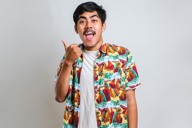 Young handsome asian man wearing casual shirt over white background with a big smile on face; pointing with hand finger to the side looking at the camera.