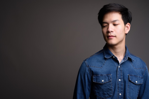 young handsome Asian man wearing denim shirt on gray