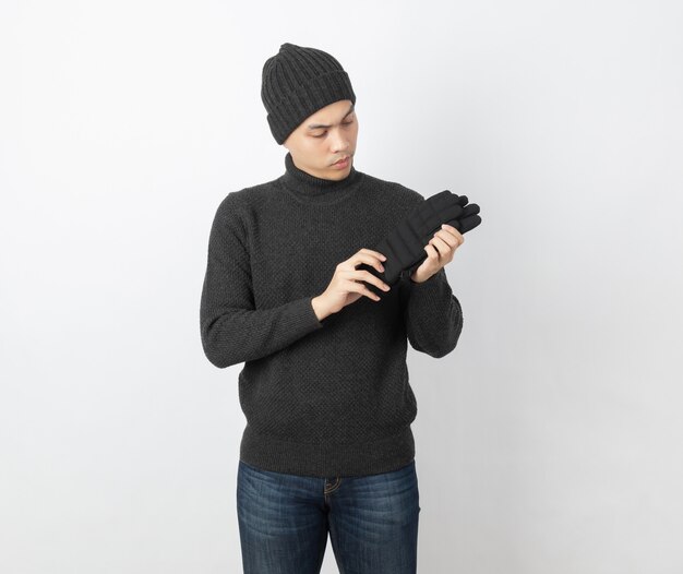 Young handsome asian man wearing grey sweater and beanie looking to her warm gloves