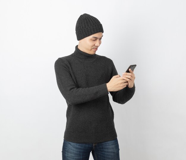 Young handsome asian man wearing grey sweater and beanie while playing smartphone with smiling