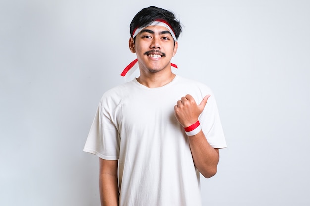 Young handsome asian man wearing red and white headband over white background with a big smile on face; pointing with hand finger to the side looking at the camera.