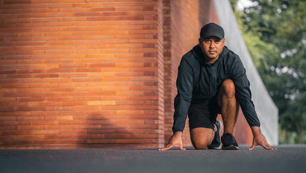 Young handsome asian man wearing sportswear doing start pose\
running under the building urban city running outdoor portraits of\
indian man jogging on the road training athlete outdoor