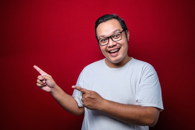 Young handsome asian man wearing white t-shirt over red background with a big smile on face, pointing with hand finger to the side looking at the camera.