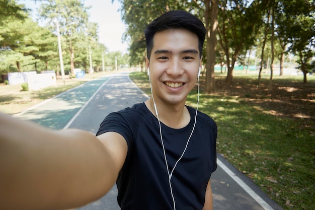 カメラに向かってセルフィーを撮ったハンサムなアジア人男性が公園で運動をしている