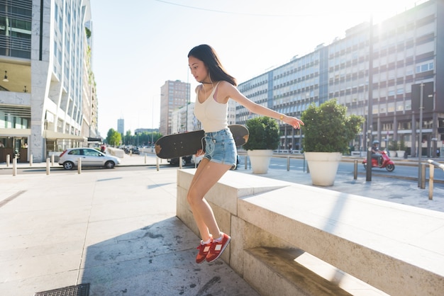 Young handsome asiatic long brown straight hair woman skater jumping down from a small wall