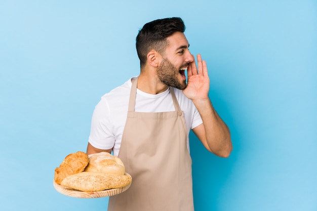 Young handsome baker man isolated shouting and holding palm near opened mouth