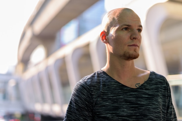 Young handsome bald man thinking against exterior of the mall