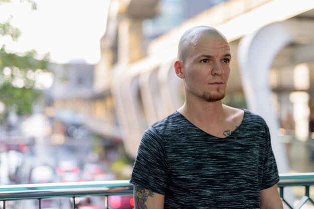 Young handsome bald man thinking on the foot bridge