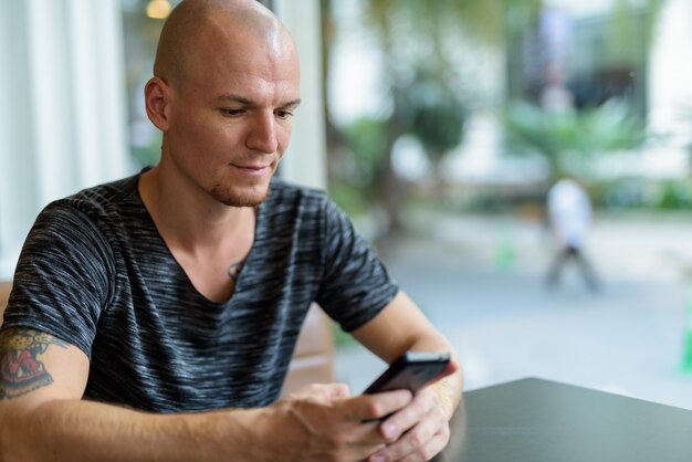 Young handsome bald man using mobile phone inside restaurant