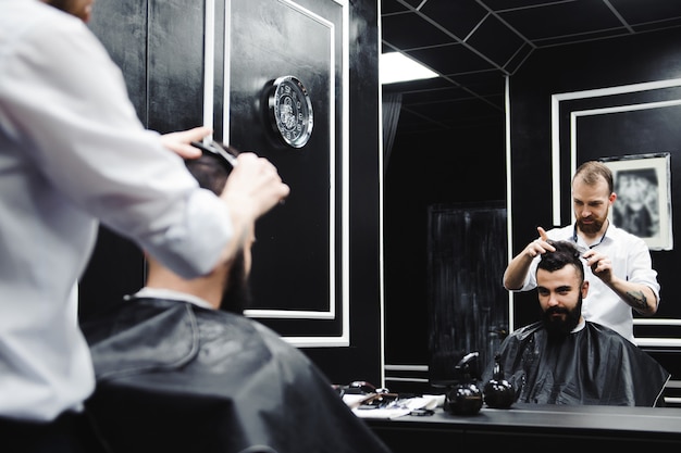 Young handsome barber making haircut of attractive man