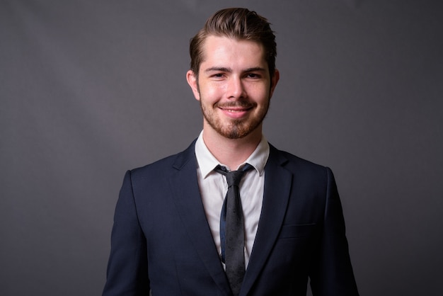 Young handsome bearded businessman against gray wall