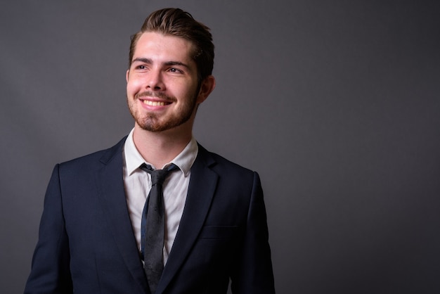 Young handsome bearded businessman against gray wall