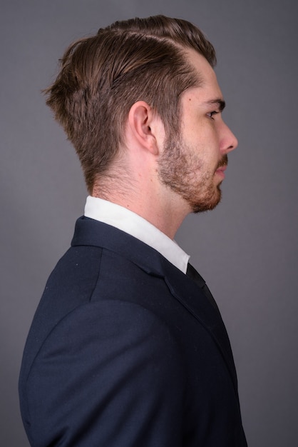 Young handsome bearded businessman against gray wall