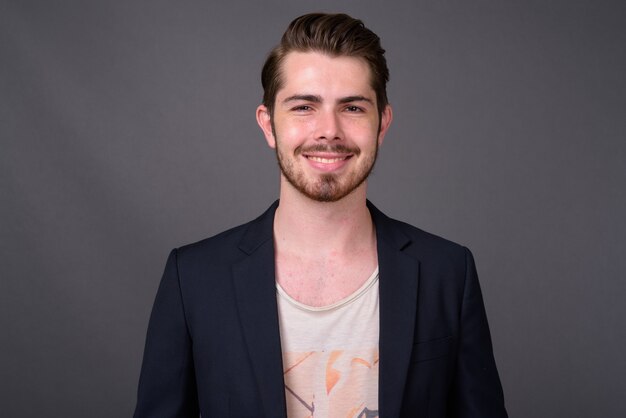 Young handsome bearded businessman against gray wall